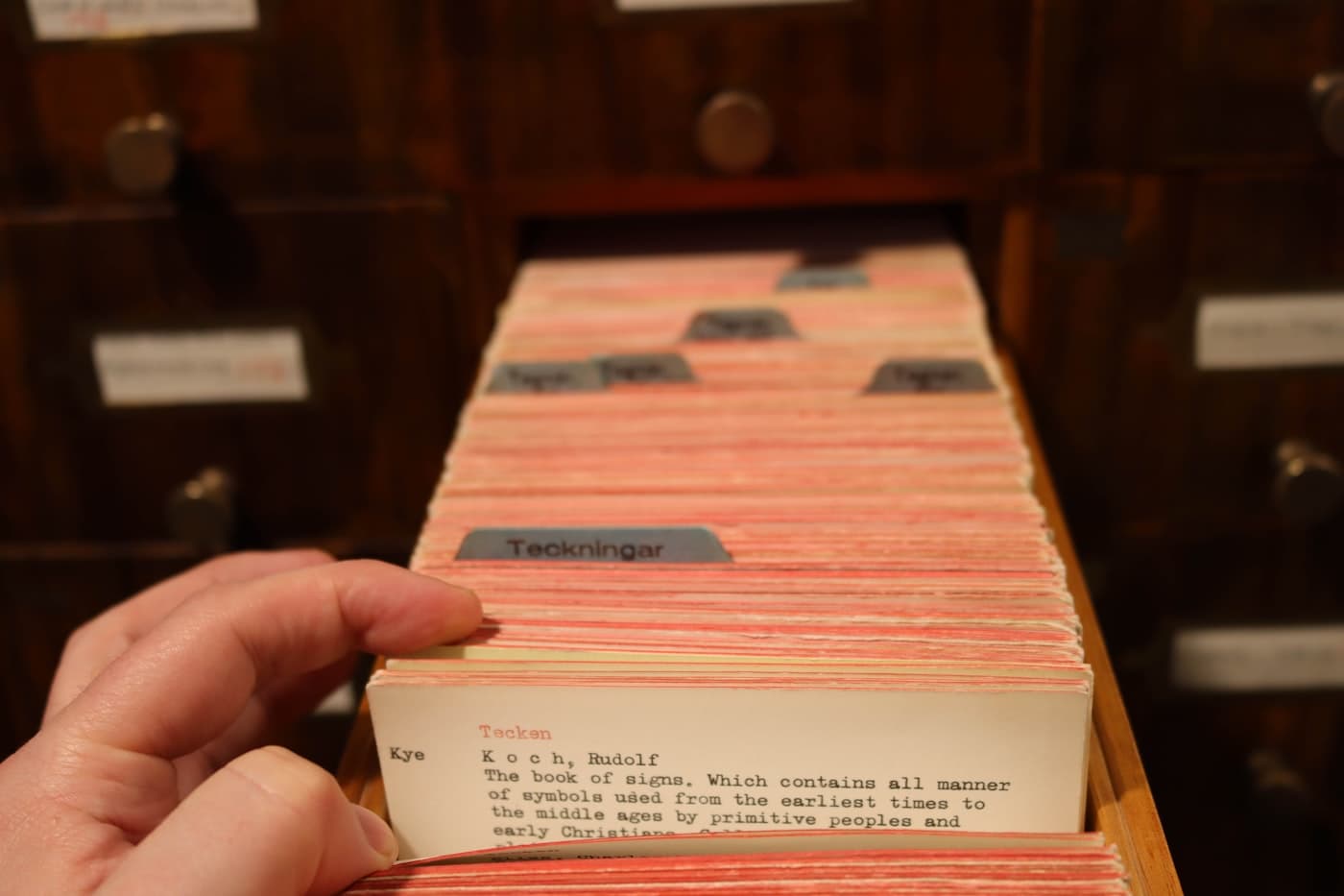 A hand withdrawing a single index card from a library catalogue drawer.